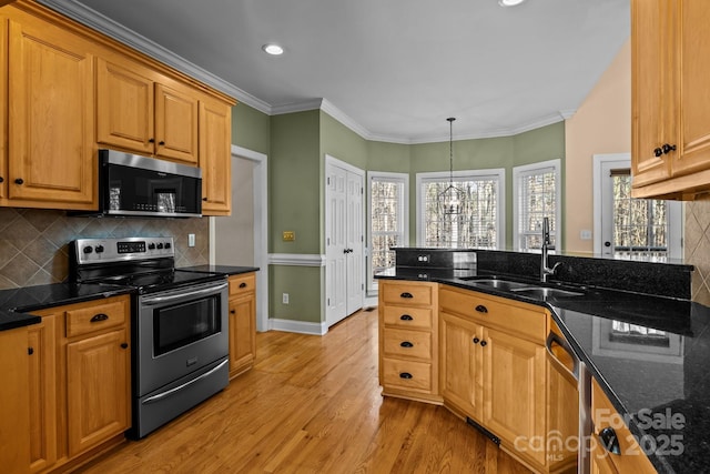 kitchen with light wood finished floors, stainless steel appliances, hanging light fixtures, a sink, and dark stone countertops