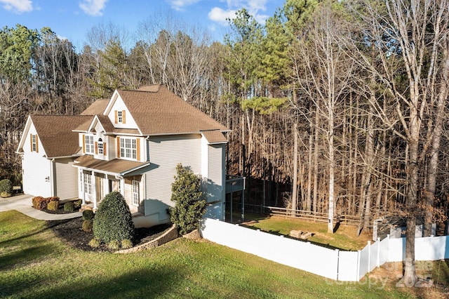 view of property exterior featuring driveway, a shingled roof, fence, and a lawn