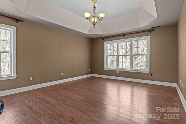 spare room with baseboards, a tray ceiling, wood finished floors, and a notable chandelier