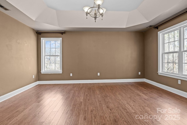 empty room featuring baseboards, visible vents, a raised ceiling, and wood finished floors