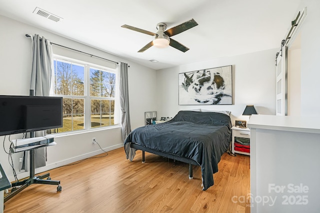 bedroom featuring light wood-type flooring, a barn door, visible vents, and baseboards