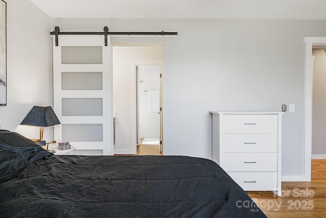 bedroom with a barn door, baseboards, and wood finished floors