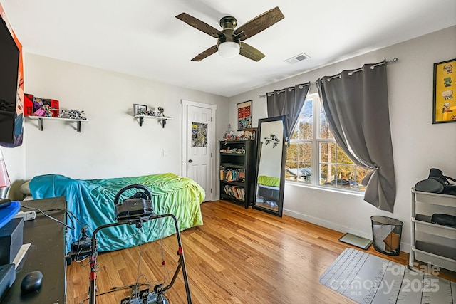 bedroom with a ceiling fan, wood finished floors, visible vents, and baseboards