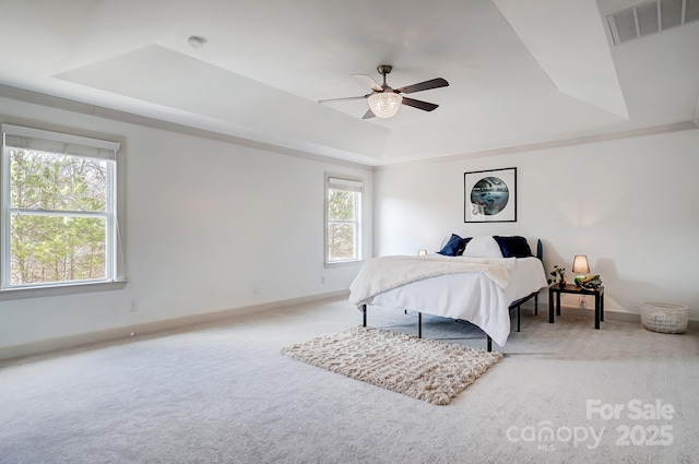 carpeted bedroom featuring a ceiling fan, visible vents, a tray ceiling, and baseboards