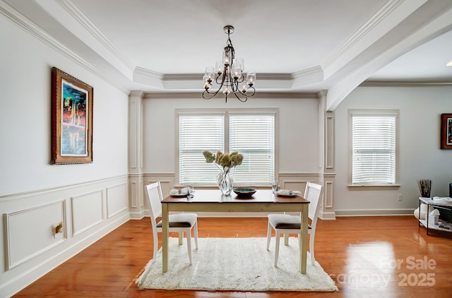 dining room with wood finished floors, a raised ceiling, a decorative wall, and an inviting chandelier