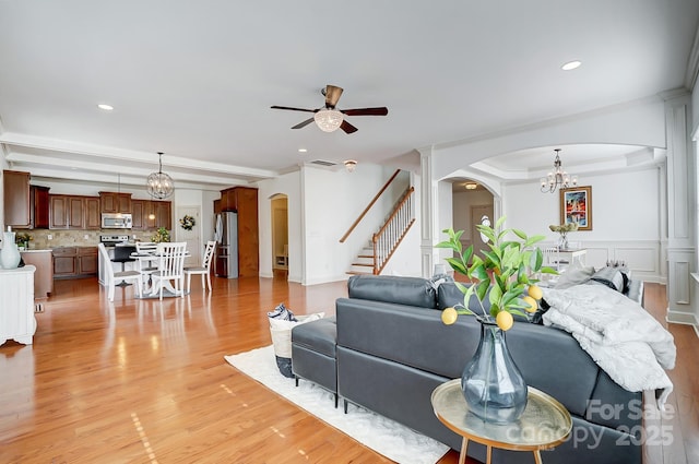 living area featuring arched walkways, light wood-style flooring, stairway, a decorative wall, and ceiling fan with notable chandelier