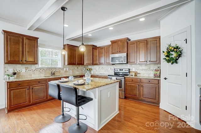 kitchen with beam ceiling, appliances with stainless steel finishes, light wood-style floors, a kitchen island, and a kitchen bar