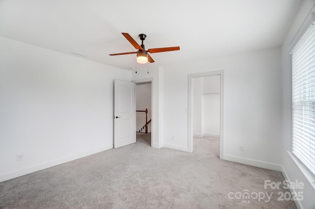 unfurnished bedroom with a ceiling fan, carpet, a walk in closet, and baseboards