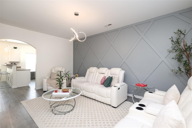 living area featuring arched walkways, an accent wall, wood finished floors, visible vents, and baseboards