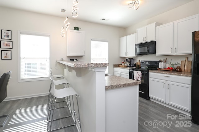 kitchen with a breakfast bar, light countertops, black appliances, white cabinetry, and pendant lighting