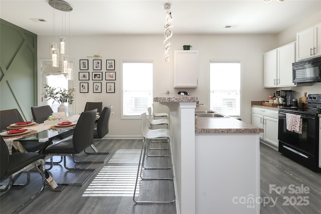 kitchen featuring pendant lighting, visible vents, white cabinets, black appliances, and a kitchen breakfast bar