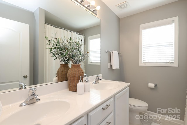 bathroom featuring visible vents, double vanity, a sink, and toilet