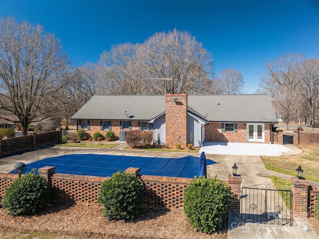 rear view of house with a fenced in pool, french doors, a patio area, fence, and driveway