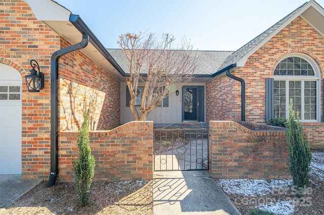 view of exterior entry featuring brick siding, an attached garage, a gate, and a shingled roof