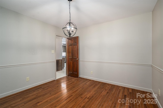 unfurnished room featuring a notable chandelier, baseboards, and wood finished floors