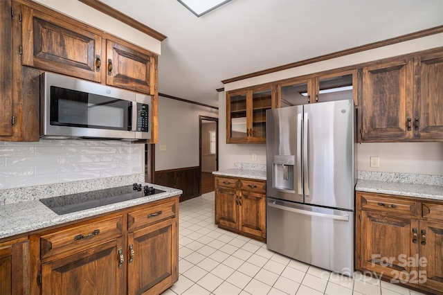 kitchen featuring light tile patterned floors, stainless steel appliances, glass insert cabinets, ornamental molding, and light stone countertops