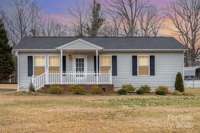 ranch-style home featuring covered porch, a front yard, and a shingled roof