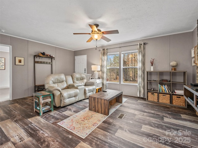 living room featuring a ceiling fan, visible vents, dark wood finished floors, and a textured ceiling