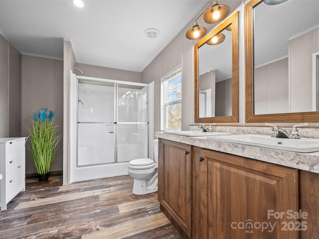 full bathroom with double vanity, wood finished floors, a stall shower, and a sink