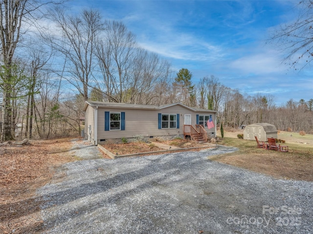 manufactured / mobile home with crawl space, a shed, gravel driveway, and an outbuilding