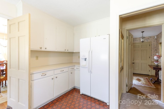 kitchen featuring wallpapered walls, white refrigerator with ice dispenser, white cabinetry, and light countertops