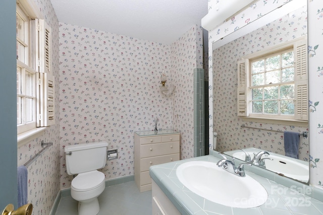 bathroom featuring wallpapered walls, toilet, vanity, baseboards, and tile patterned floors