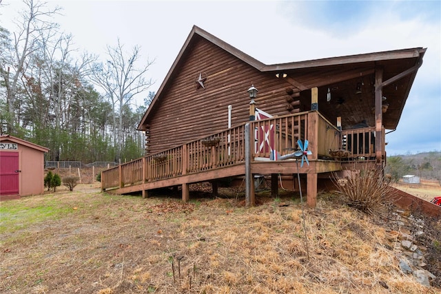 back of house with a deck, log exterior, a storage unit, and an outdoor structure