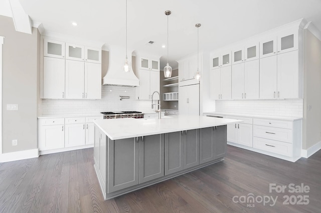 kitchen featuring light countertops, a center island with sink, glass insert cabinets, and white cabinetry