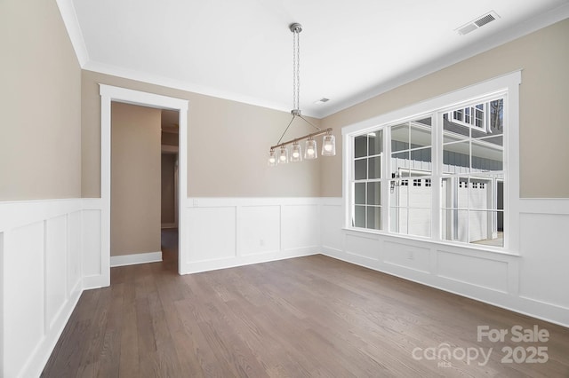 unfurnished dining area featuring dark wood-style floors, ornamental molding, wainscoting, and visible vents