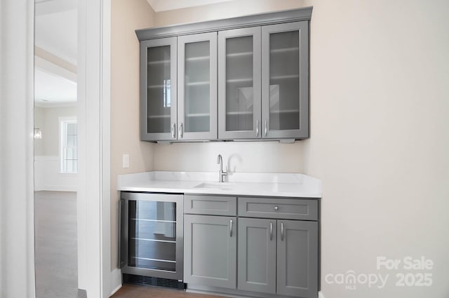 bar featuring a wainscoted wall, wine cooler, and a sink