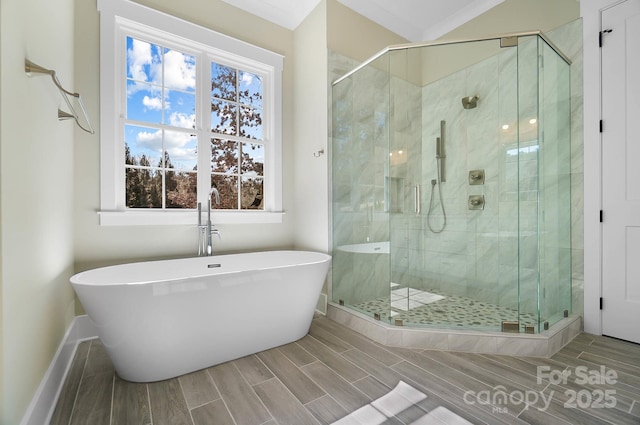 bathroom with baseboards, wood finish floors, a freestanding tub, and a shower stall