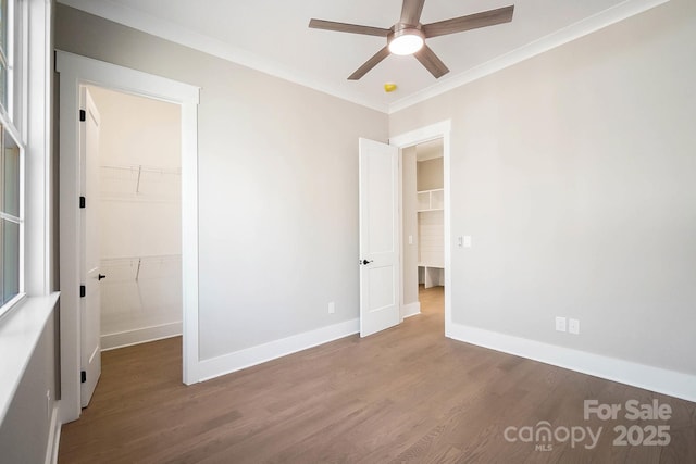 unfurnished bedroom featuring crown molding, dark wood finished floors, a spacious closet, and baseboards