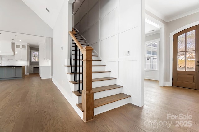 staircase featuring baseboards, a decorative wall, wood finished floors, and crown molding