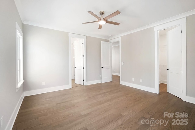 unfurnished bedroom featuring baseboards, a spacious closet, wood finished floors, and crown molding