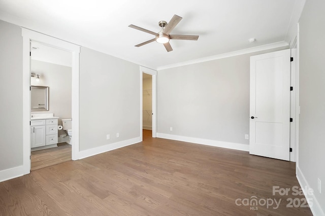 unfurnished bedroom featuring baseboards, light wood-style floors, ornamental molding, a walk in closet, and ensuite bath