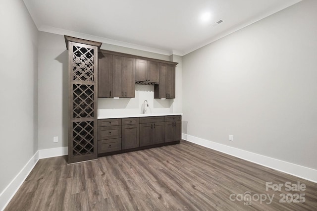 bar featuring crown molding, a sink, baseboards, and wood finished floors