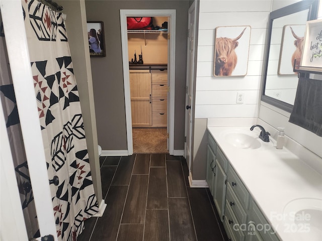 bathroom with wood finish floors, vanity, baseboards, a spacious closet, and a shower with curtain