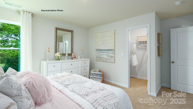 bedroom with a spacious closet, visible vents, baseboards, and light carpet
