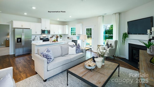 living area with dark wood finished floors, baseboards, a glass covered fireplace, and recessed lighting