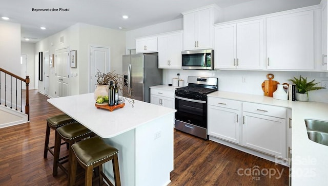 kitchen featuring appliances with stainless steel finishes, a kitchen breakfast bar, dark wood-type flooring, and white cabinetry