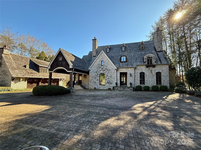 french country style house with decorative driveway and a chimney