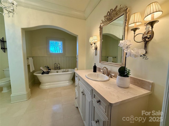 full bath with a soaking tub, toilet, ornamental molding, wainscoting, and vanity