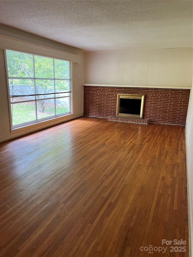 unfurnished living room featuring a brick fireplace, a textured ceiling, and wood finished floors