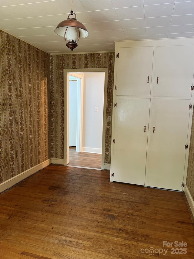 empty room featuring wallpapered walls, baseboards, and wood finished floors