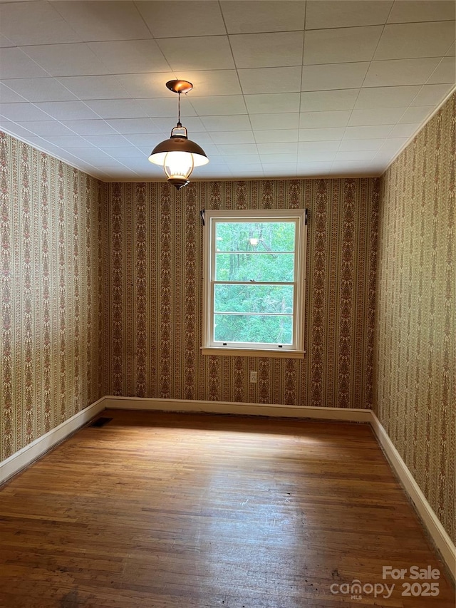 spare room featuring wallpapered walls, baseboards, and wood finished floors