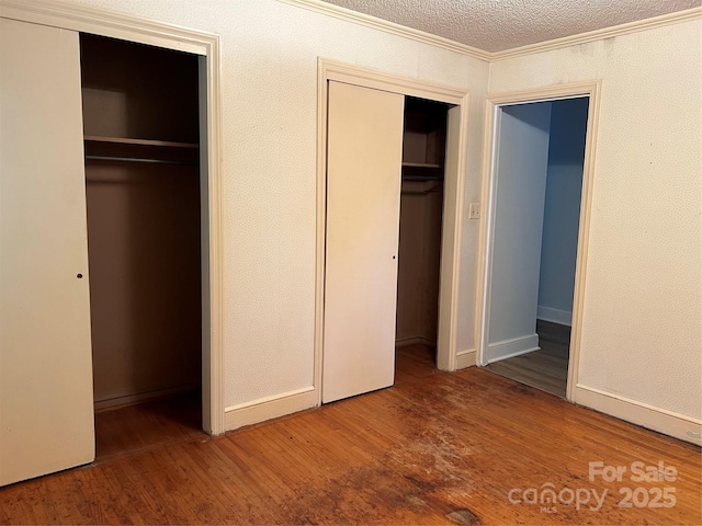 unfurnished bedroom with crown molding, a textured ceiling, two closets, and wood finished floors