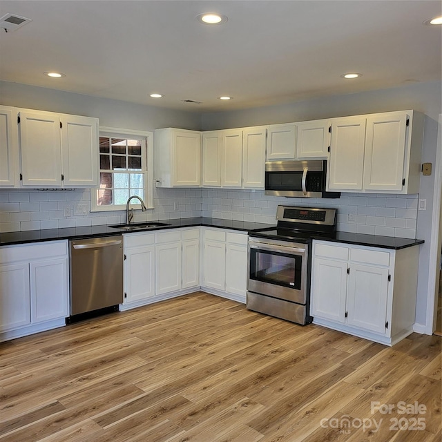 kitchen with white cabinets, dark countertops, stainless steel appliances, light wood-style floors, and a sink