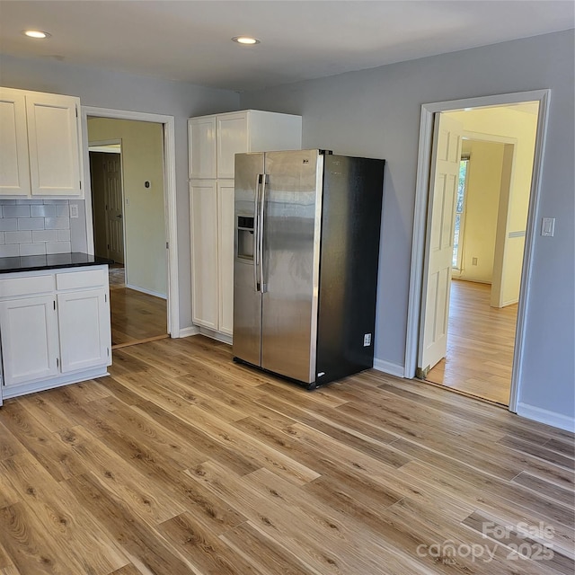 kitchen with dark countertops, light wood-style floors, stainless steel refrigerator with ice dispenser, and white cabinets