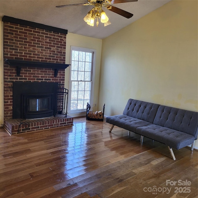 living area featuring a fireplace, ceiling fan, vaulted ceiling, a textured ceiling, and wood finished floors