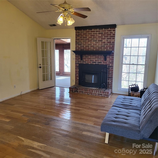 living room with visible vents, a ceiling fan, a brick fireplace, wood finished floors, and baseboards